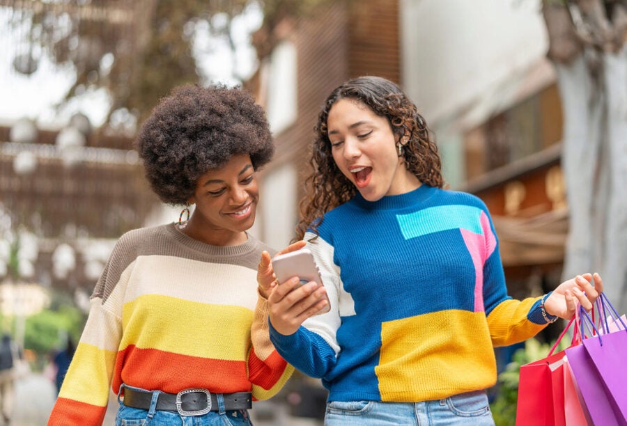 Two friends out shopping and looking at something on a smartphone together to illustrate the process of customer referrals