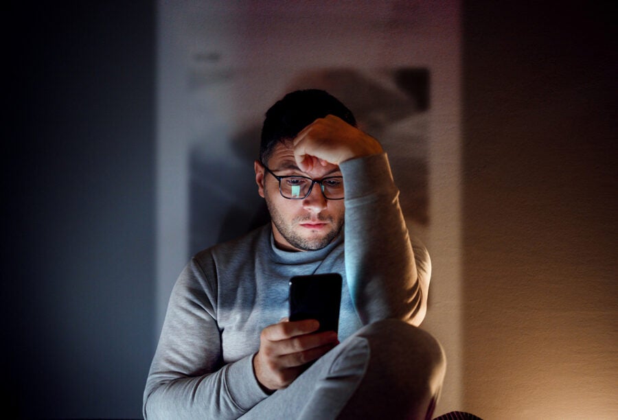 Man sitting in a dark room while using his phone and seeing social media misinformation