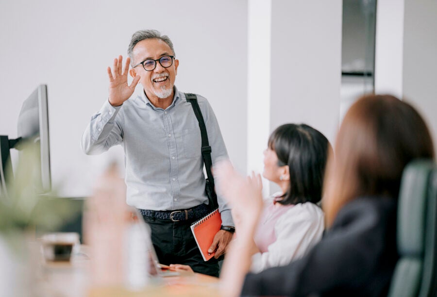 Older man smiling and waving to his colleagues as he heads to retirement