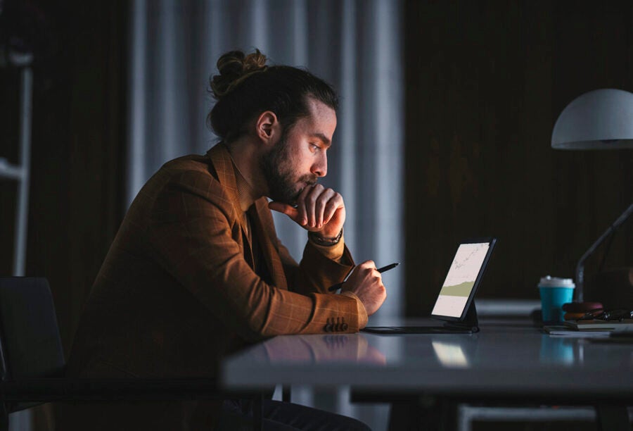 Man in a dark room analyzing stocks on his tablet screen