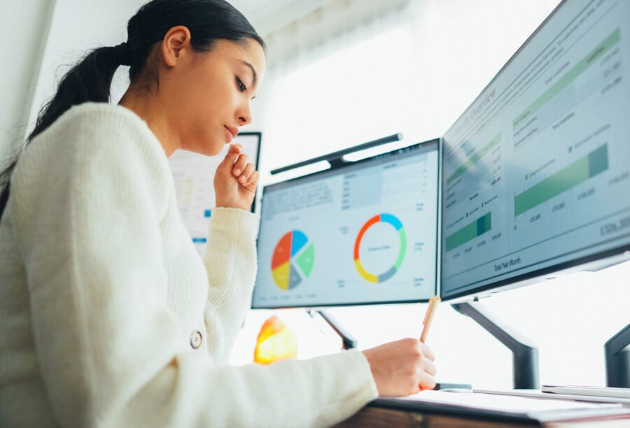 Woman working at a desk with computers screens showing financial information to show the potential of AI-powered financial advice