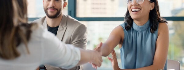 Woman shaking hands with a recruiter while another candidate is sitting next to her, showing how being a second choice hire can affect someone's sense of belonging at work