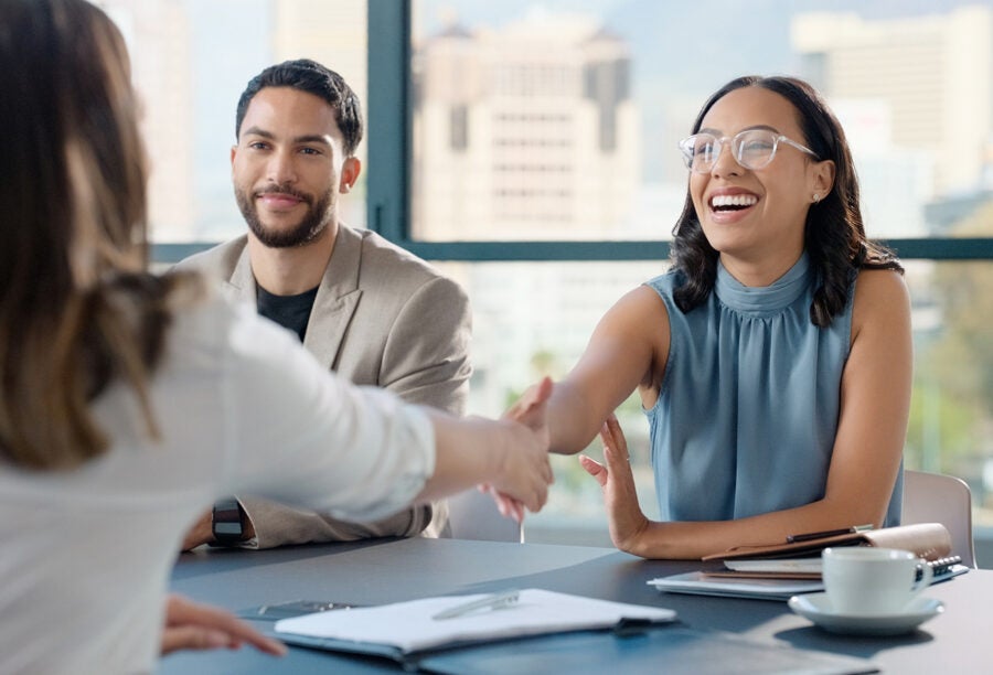 Woman shaking hands with a recruiter while another candidate is sitting next to her, showing how being a second choice hire can affect someone's sense of belonging at work