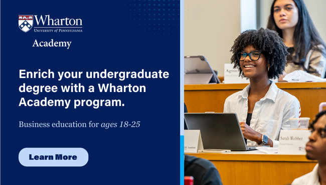 A student with glasses smiles while holding a laptop in a lecture hall, surrounded by a small group of peers. The image promotes Wharton Academy’s program aimed at enriching undergraduate education for individuals aged 18-25. Click to learn more.