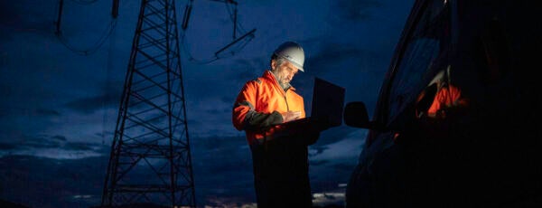 Electrical engineer in an orange uniform working outside at night to show the impact of AI energy consumption