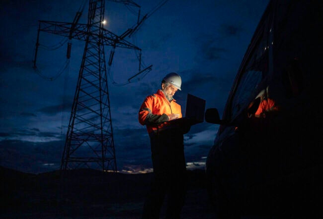 Electrical engineer in an orange uniform working outside at night to show the impact of AI energy consumption