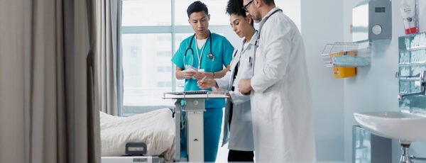 Doctors standing at the foot of a hospital bed. Is corporatization why hospitals are so expensive?