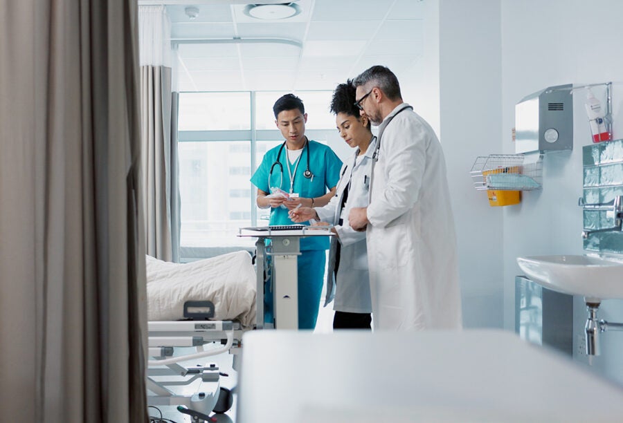 Doctors standing at the foot of a hospital bed. Is corporatization why hospitals are so expensive?