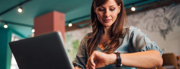 Woman looking at her watch while working on her laptop