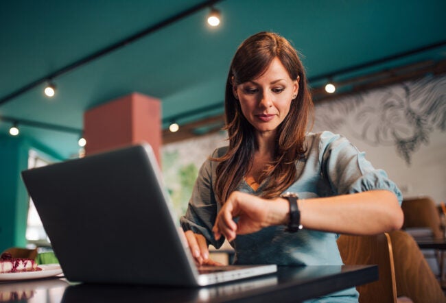 Woman looking at her watch while working on her laptop