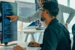 Two employees looking at code on a computer screen to show how AI is being integrated at work