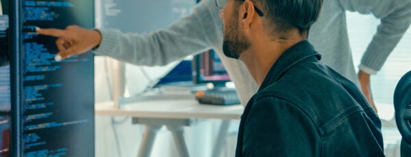 Two employees looking at code on a computer screen to show how AI is being integrated at work