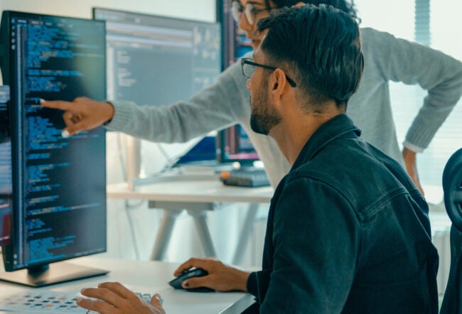 Two employees looking at code on a computer screen to show how AI is being integrated at work