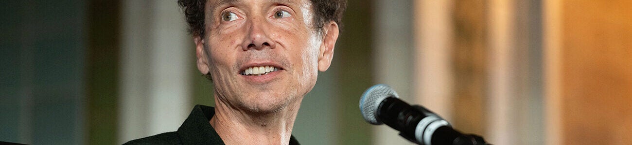 Malcolm Gladwell in a black shirt speaking into a microphone