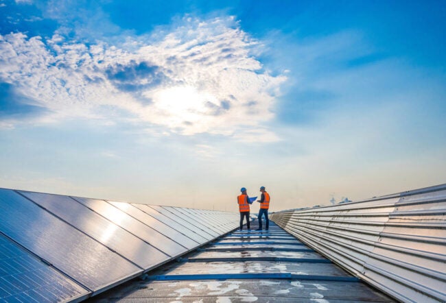 Two technicians in distance discussing between long rows of photovoltaic panels. Why should companies care about their carbon emissions?