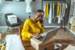 An entrepreneur sitting in their workspace and smiling as they plan their fashion business. Why are some societies more entrepreneurial?