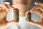 Person holding up two uneven stacks of coins to show how income inequality in America is hurting our collective happiness