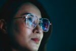 Closeup of a woman's face with a computer screen reflected in her glasses to illustrate the state of AI regulation