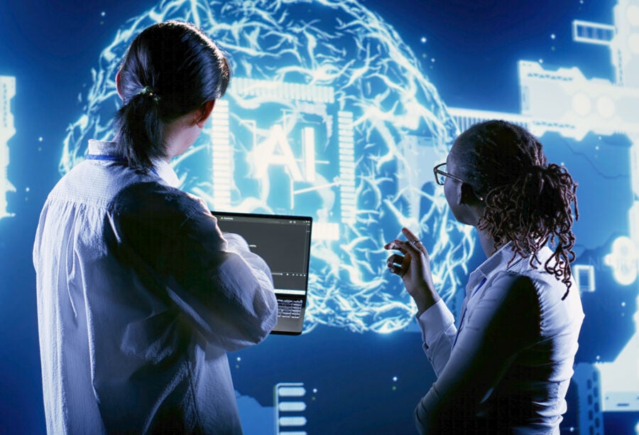 Two employees looking at a large screen that reads "AI"