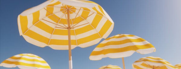 Yellow and white striped beach umbrellas against a clear blue sky, evoking a sunny, summer day at the beach.