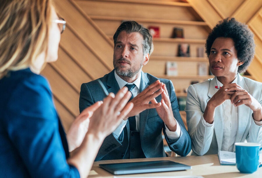 An employee speaking animatedly in the office while two coworkers listen with mixed reactions. Can pride make you look like an incompetent worker?