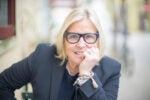 Amy Errett in a suit jacket and glasses with her chin propped up in her hand