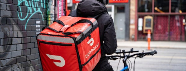 A DoorDash food delivery courier on a bike facing restaurants across the street