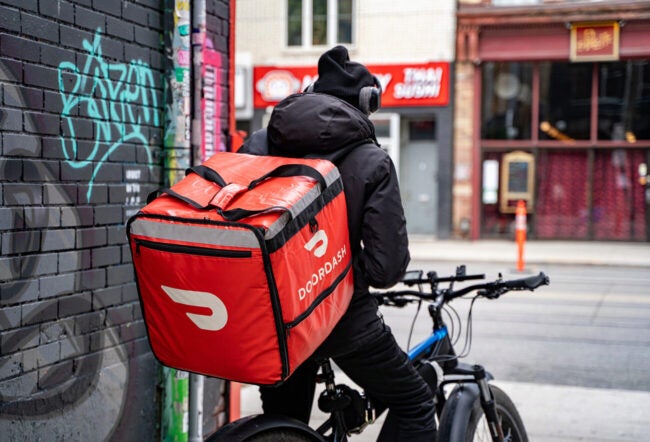 A DoorDash food delivery courier on a bike facing restaurants across the street