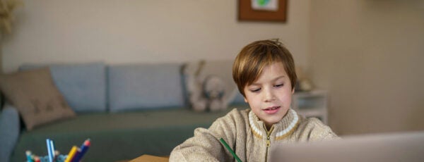 Young child doing homework in a notebook while using a laptop