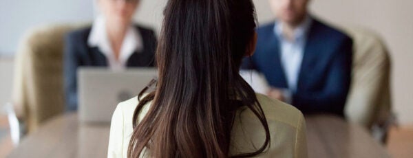 Female job candidate sitting with her back to the camera as she faces two interviewers. How do we increase the number of women in leadership?