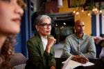 Businesswoman in her 40s sitting with colleagues with serious expression.
