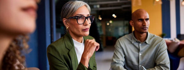 Businesswoman in her 40s sitting with colleagues with serious expression.