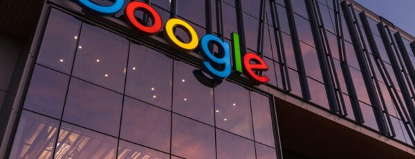 The image shows a modern glass building with the Google logo prominently displayed on the facade. The sky reflects in the windows, creating a warm ambiance.
