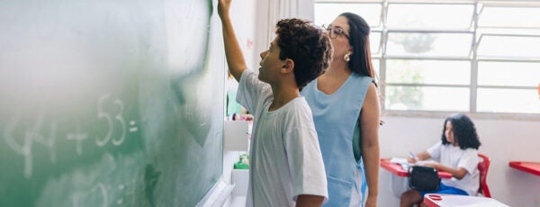 Elementary school student doing math on the chalkboard with his teacher