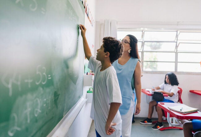 Elementary school student doing math on the chalkboard with his teacher
