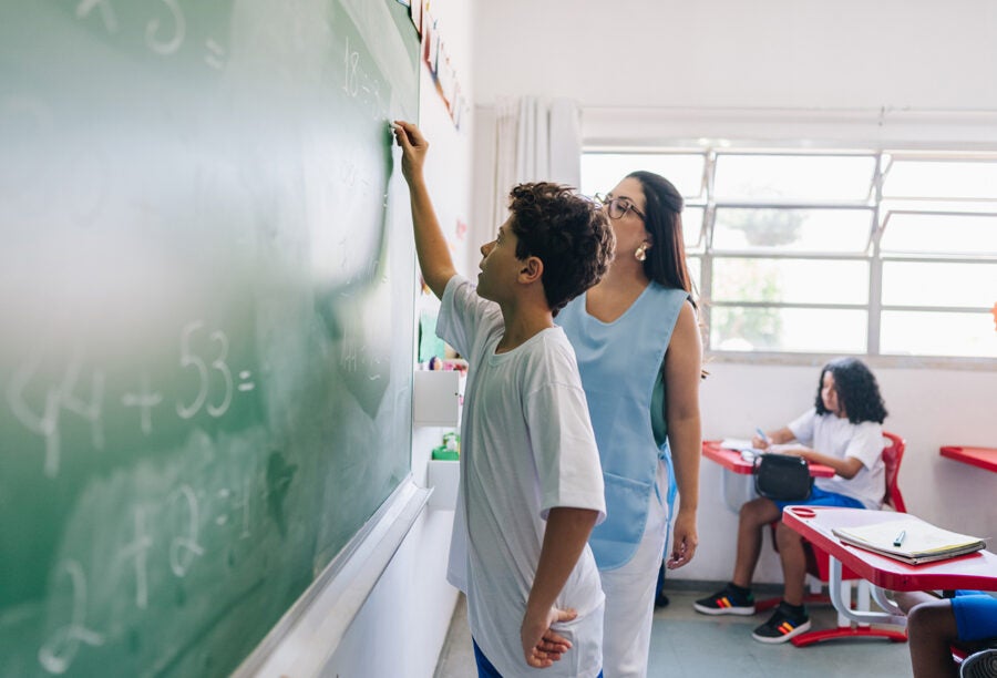 Elementary school student doing math on the chalkboard with his teacher