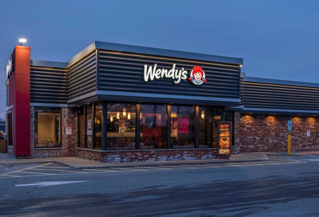 A Wendy's restaurant exterior at dusk, featuring the illuminated logo with red and white signage on a modern building facade.