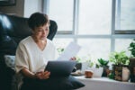 Senior woman looking over a document with her computer in her lap