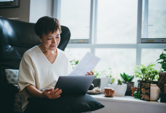 Senior woman looking over a document with her computer in her lap