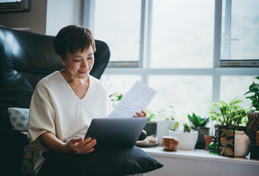 Senior woman looking over a document with her computer in her lap