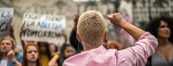 A protester with their fist raised facing a crowd of demonstrators on the street