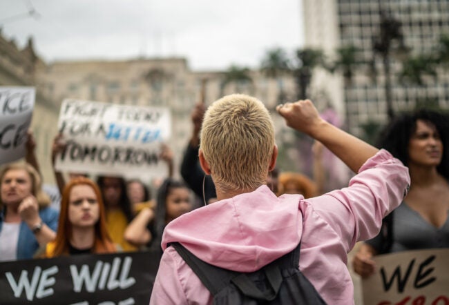 A protester with their fist raised facing a crowd of demonstrators on the street