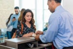 The mid adult woman watches as the male bank teller counts out the cash she has just taken out of her savings account.