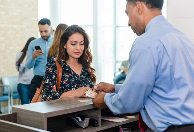 The mid adult woman watches as the male bank teller counts out the cash she has just taken out of her savings account.
