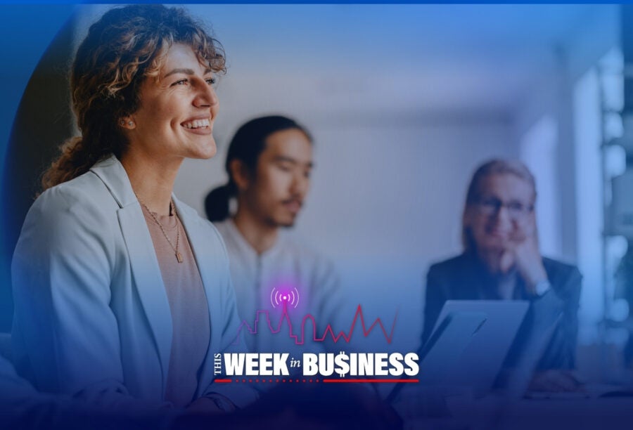 A group of professionals smiling in a meeting room with a text overlay that reads "This Week in Business," featuring a graphical line representing economic activity.