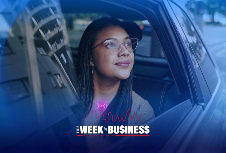 A person wearing glasses looks out of a car window with a reflective building visible. The image features a graphic that reads "This Week in Business" with a skyline and signal icon.