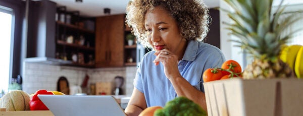 Woman using her laptop in the kitchen while surrounded by fresh groceries and produce in the kitchen