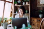 Woman working on her laptop in a home office full of plants