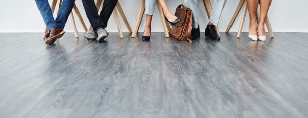 A group people sitting in a row waiting for an interview with their faces cropped out of the shot