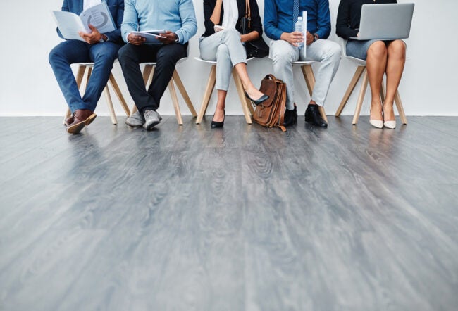 A group people sitting in a row waiting for an interview with their faces cropped out of the shot